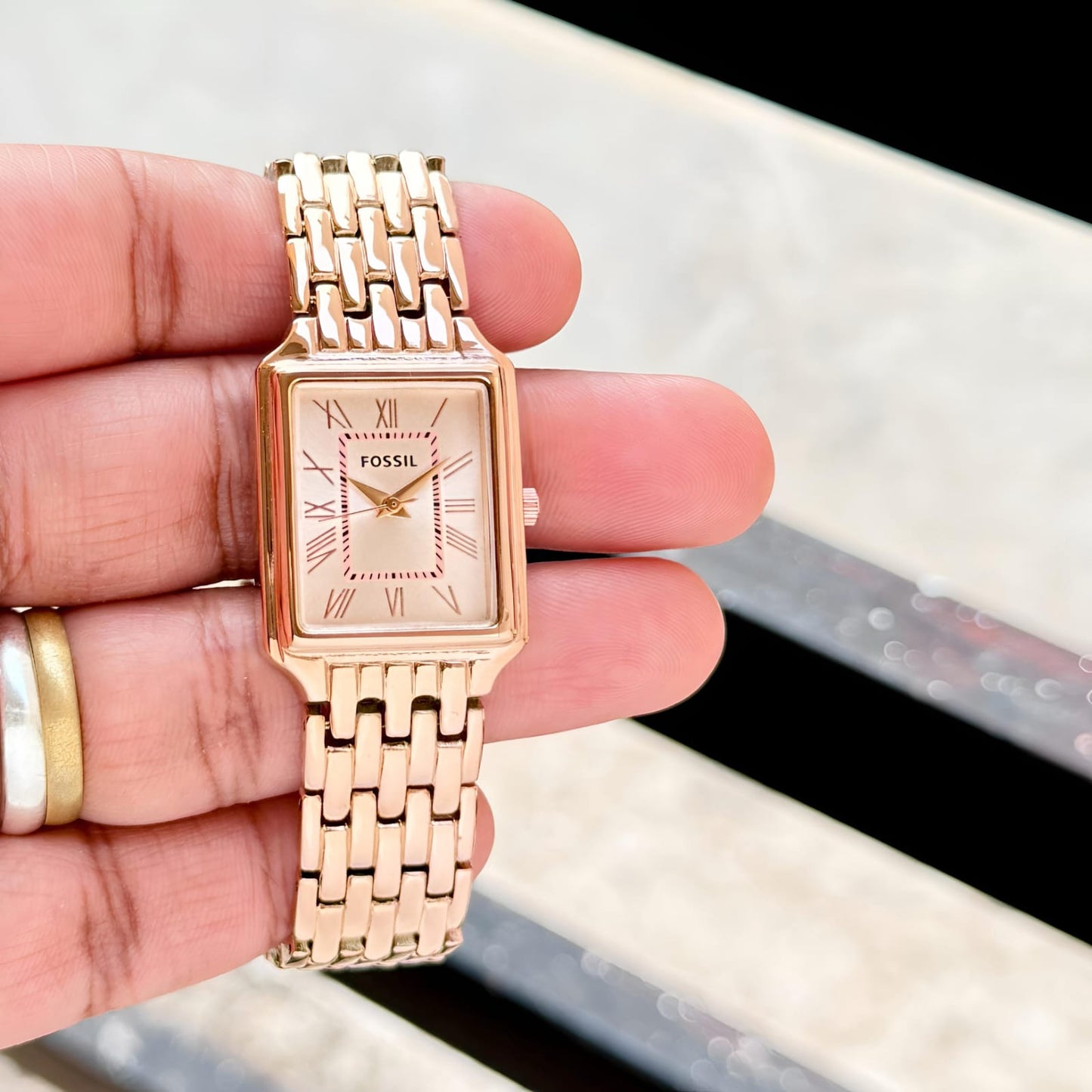 Rose gold Fossil watch held in a hand with a blurred background